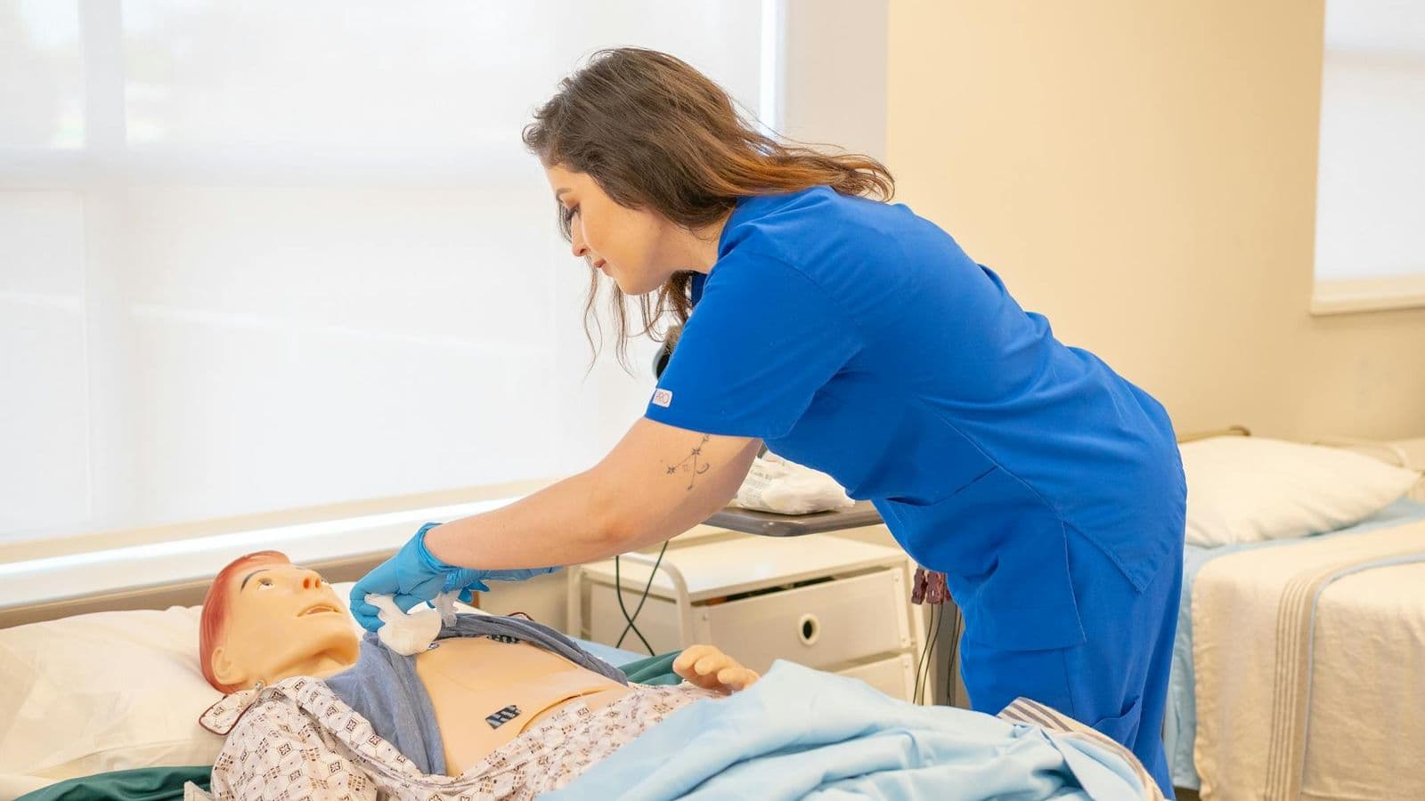A nurse in blue scrubs trains on a medical dummy in a healthcare facility.