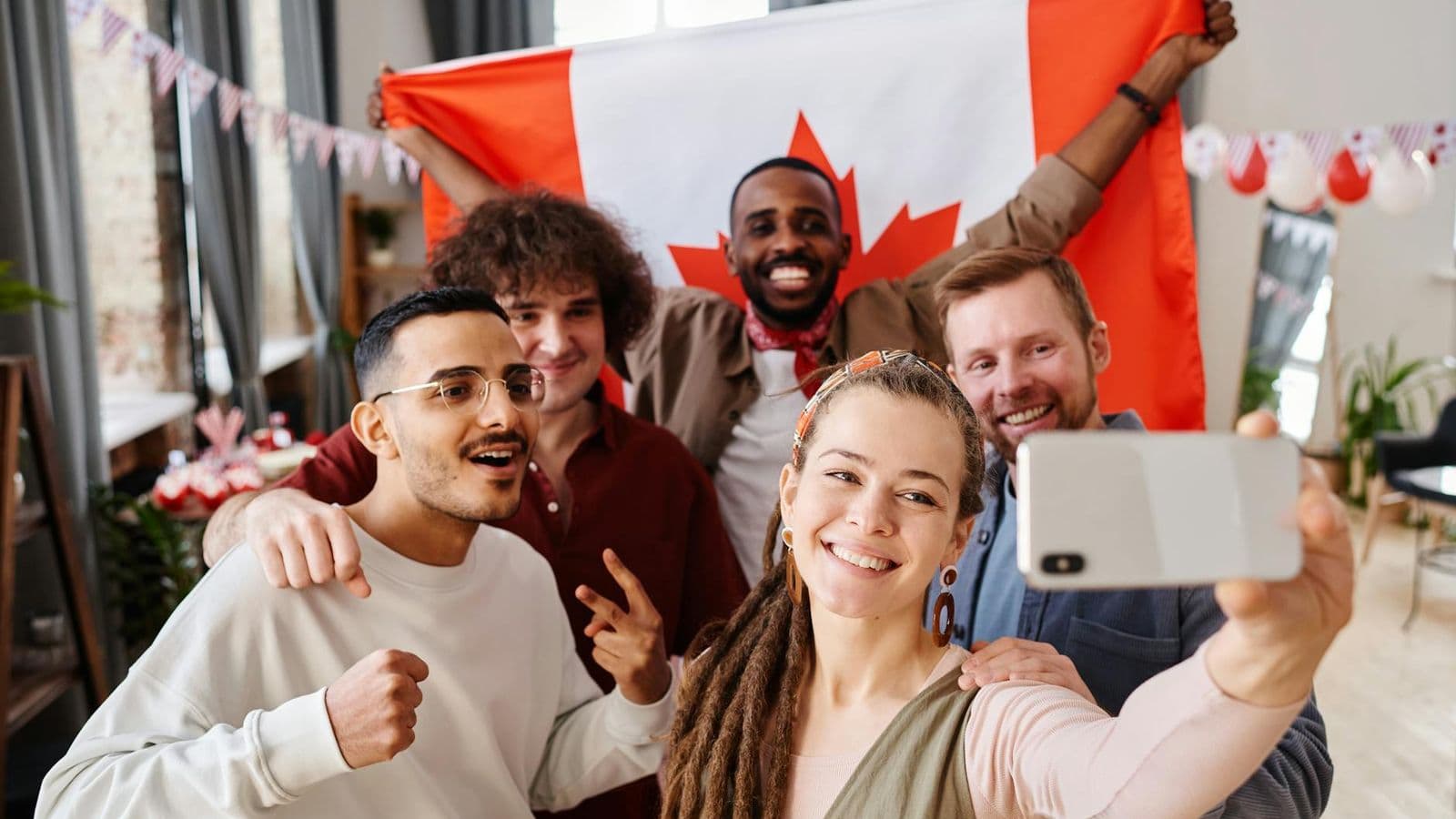 A diverse group of friends celebrating Canada Day with a joyful selfie indoors.
