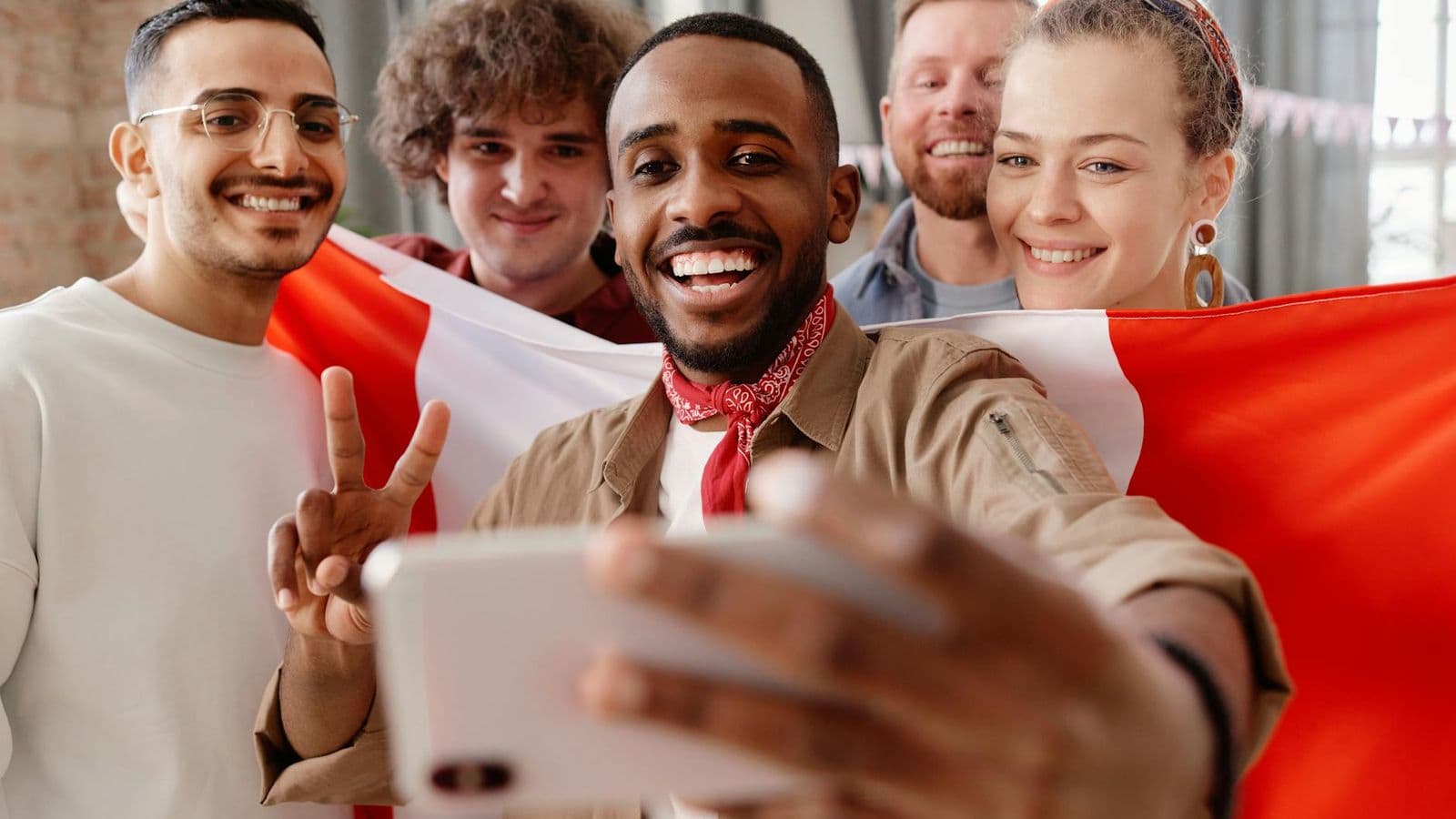 Diverse group of friends taking a joyful selfie while celebrating indoors with a flag.